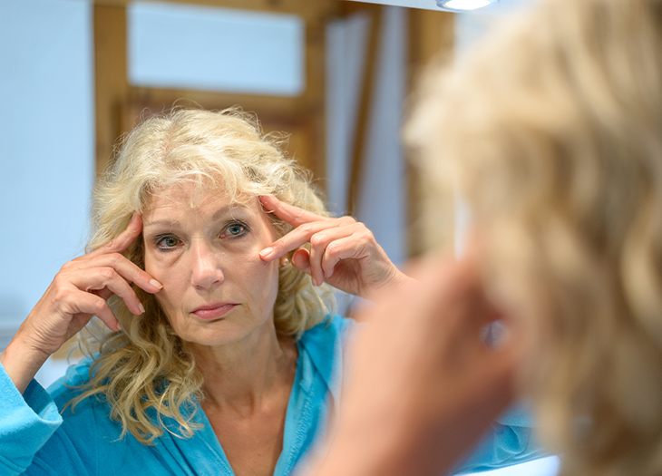 Woman holding eyes apart looking in a mirror